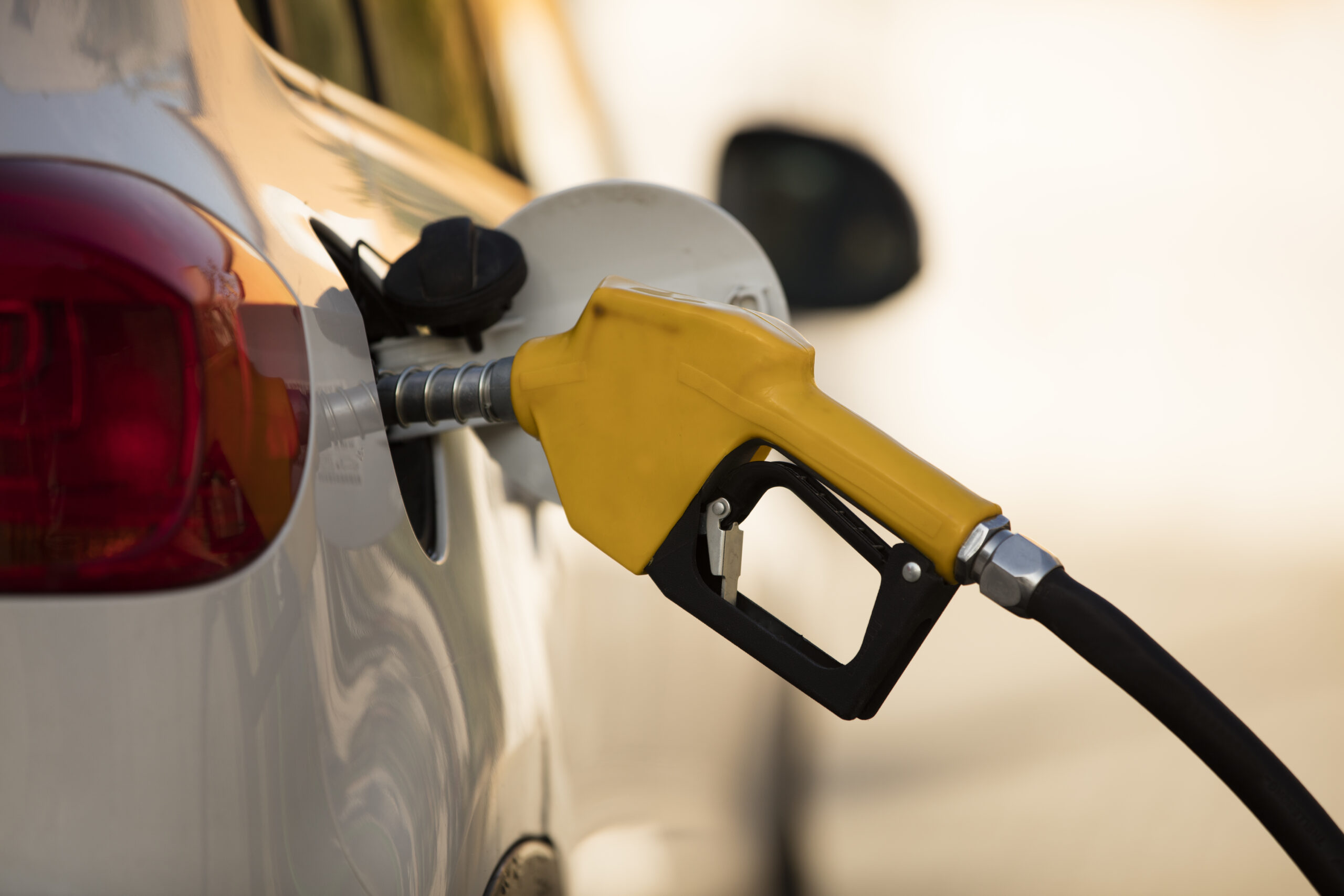 Close-up of a yellow gas pump nozzle inserted into a car's fuel filler neck at a gas station